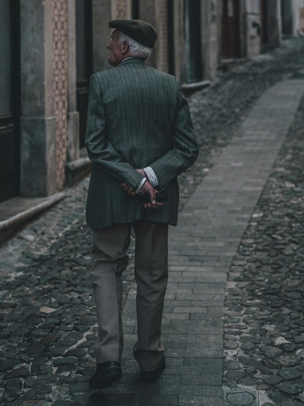Homem de casaco verde caminhando na calçada de tijolos entre edifícios de concreto durante o dia
