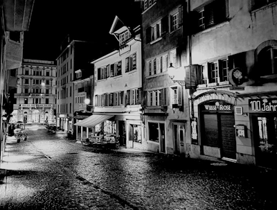 Black and white photograph of an old street with cobblestones and vintage lamps