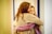 Two individuals embrace in a hug, showing close emotional connection. Both are dressed in casual clothing, one wearing a beige sweater and the other in a purple one. The background is softly lit with yellow tones, likely indoors.