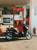 Motorcycle parked beside iconic oil brand containers like Liqui Moly and Agip