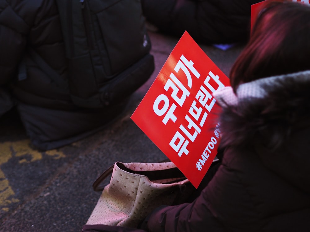 person holding red and white text signage