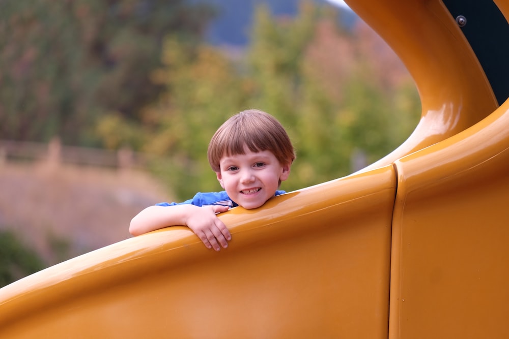 smiling boy sitting on orange slide during daytime