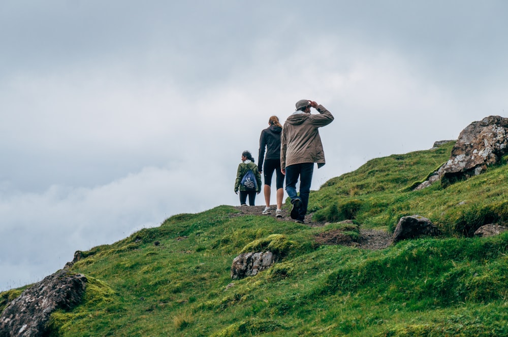 three person walking on green cliff