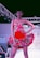 A model confidently walks down a runway wearing a vibrant red dress adorned with floral patterns. The dress features a strapless top and a flared skirt accentuated with multicolored flowers. Overhead lighting highlights the model and creates a dramatic atmosphere on the fashion show stage.
