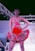 A model confidently walks down a runway wearing a vibrant red dress adorned with floral patterns. The dress features a strapless top and a flared skirt accentuated with multicolored flowers. Overhead lighting highlights the model and creates a dramatic atmosphere on the fashion show stage.