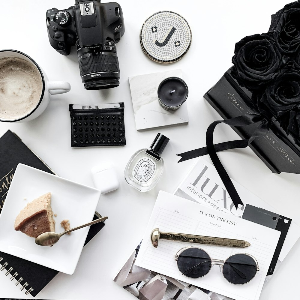 flat lay photography of DSLR camera, teacup, black rose flowers, and sunglasses
