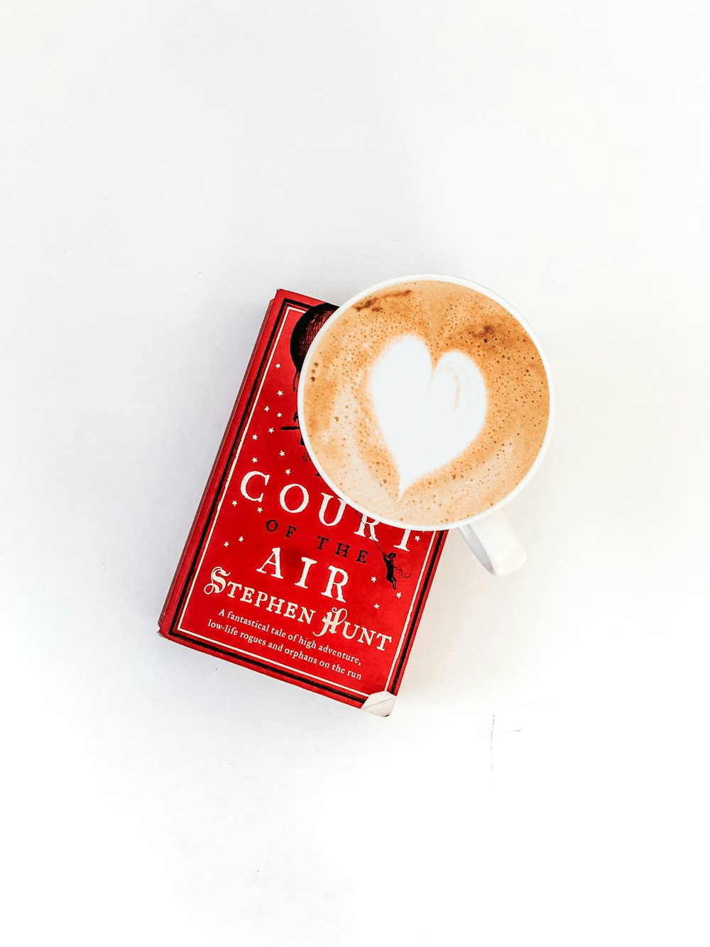 round white ceramic cup on top of red Court Air by Stephen Hunt book