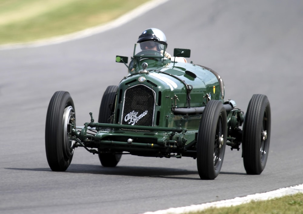 person driving vintage green convertible car on race track during daytime