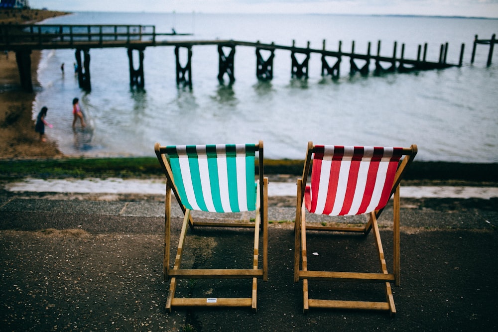 two green, white, and red striped deckchairs near body of water