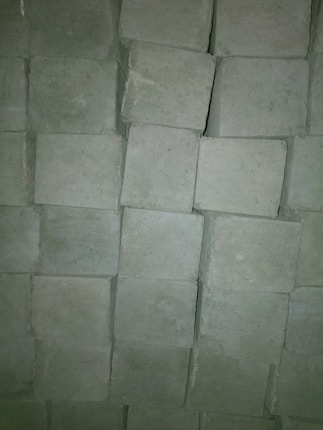 A close-up view of a stack of grayish cement blocks arranged in an orderly fashion. The blocks have a rough texture and are slightly irregular in shape, creating a pattern through their arrangement.