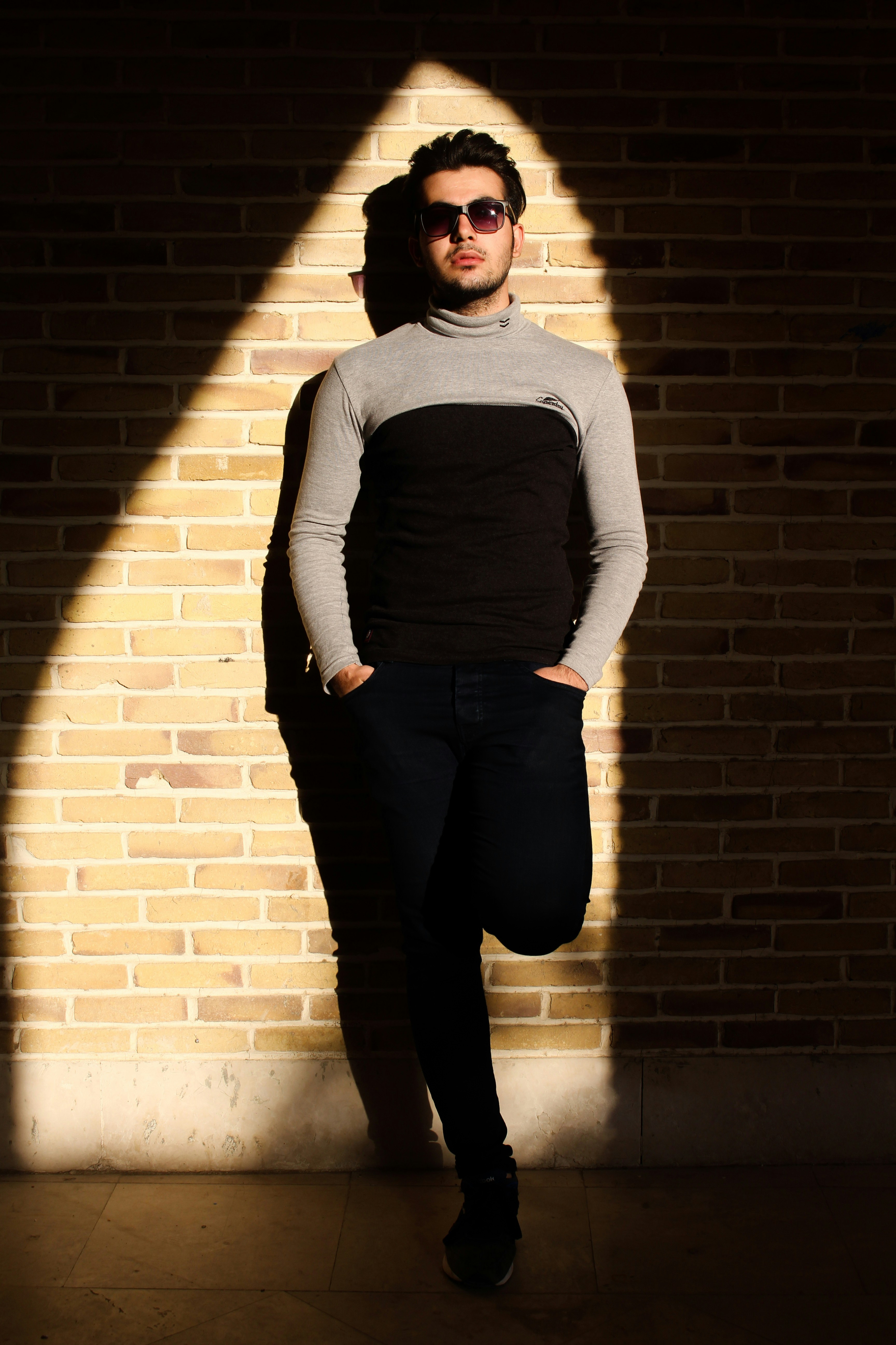 man in black and gray sweater standing and leaning on brick wall