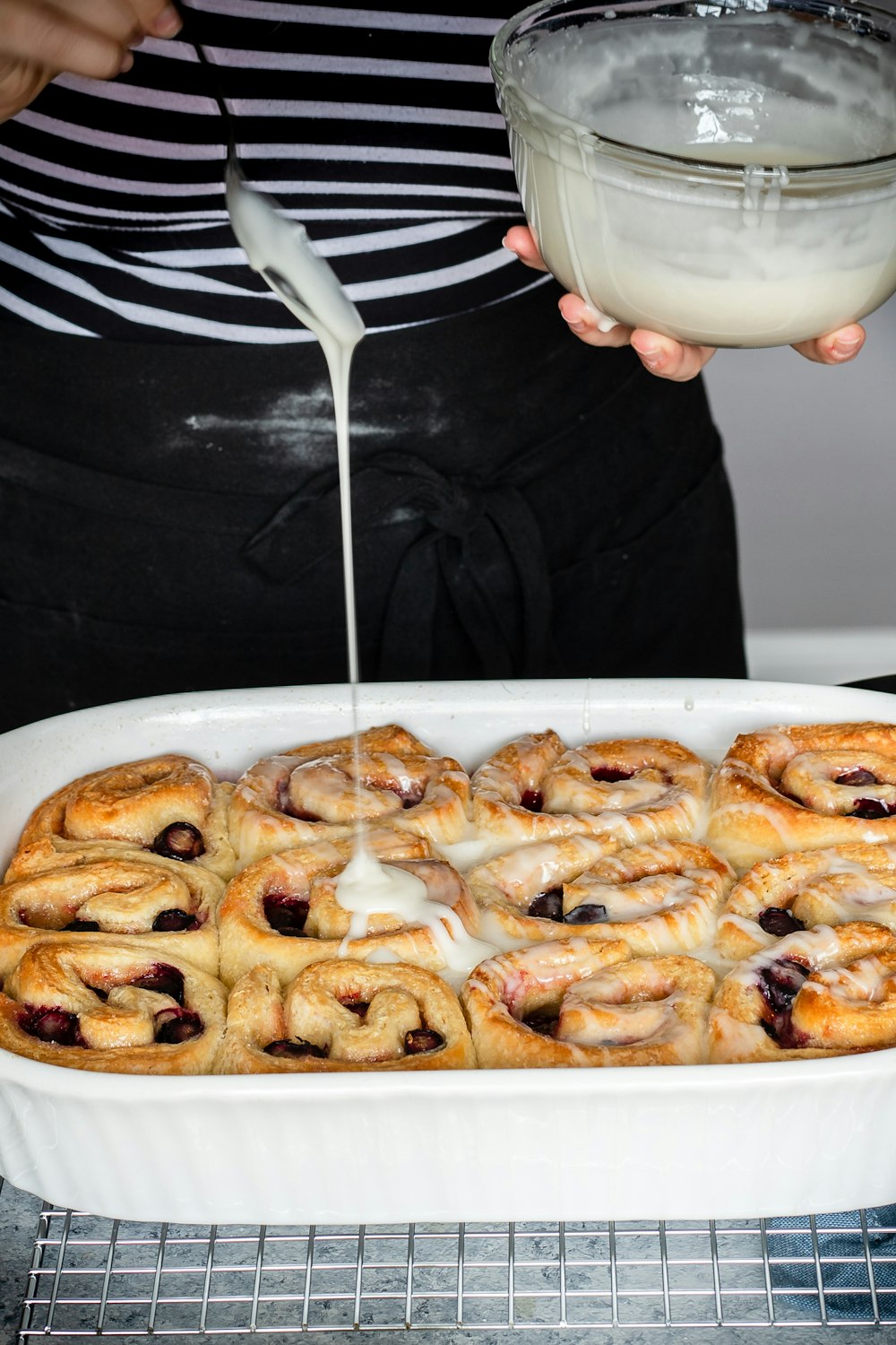 person pouring white cream sauce on rolled cake in baking dish