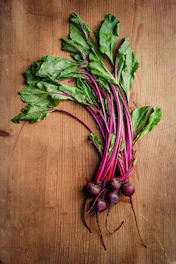 Fresh burdock roots with green leaves arranged on natural wood.
