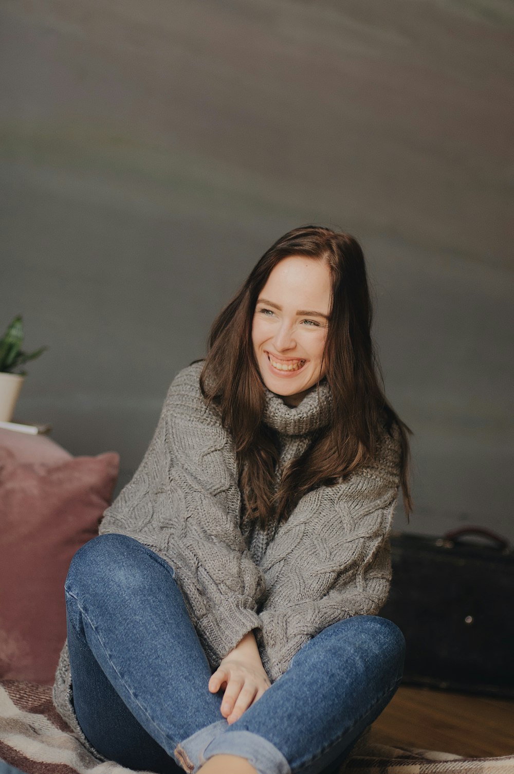 woman sitting on floor wearing gray sweater and blue denim fitted jeans