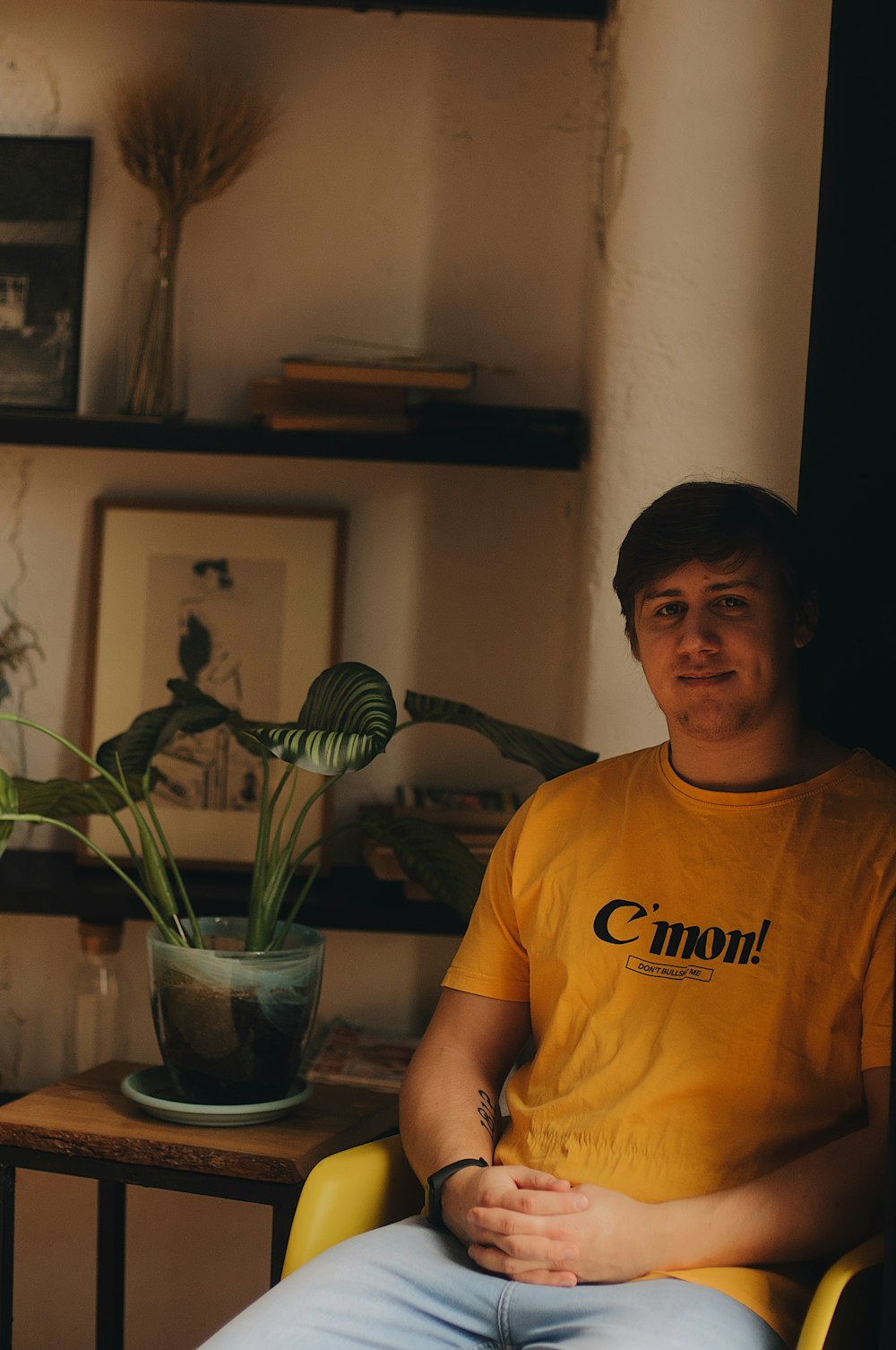 man in yellow shirt sitting inside room beside potted green leaf plant