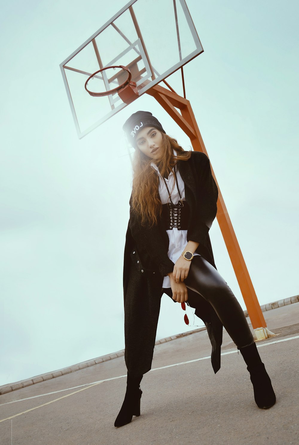 woman in black coat taking pose in front of basketball hoop during daytime