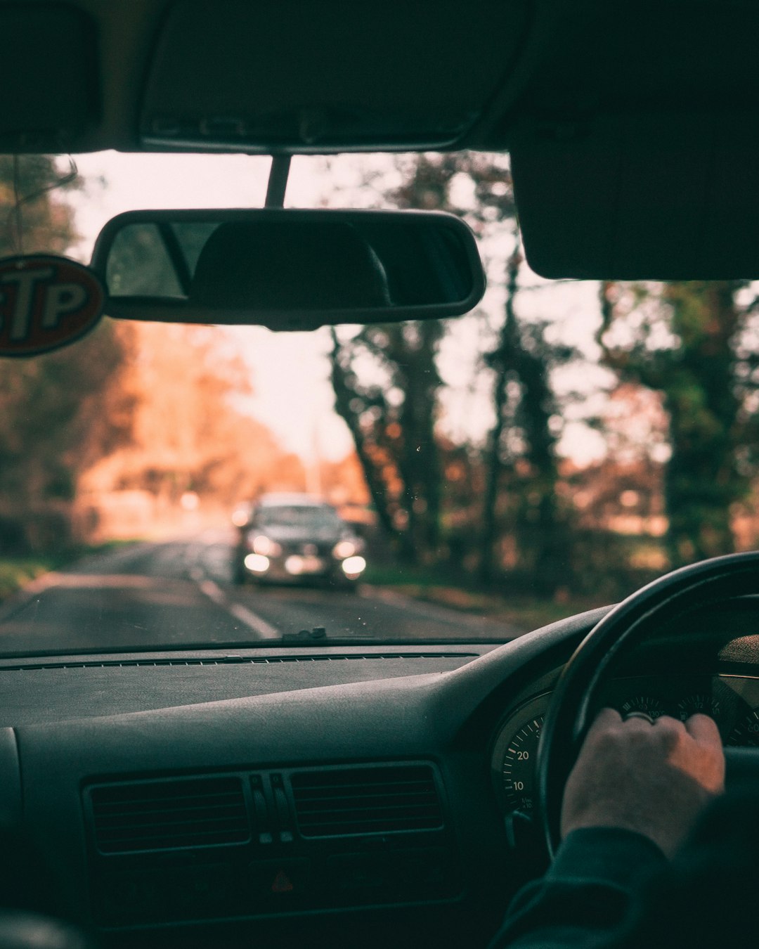 person inside car driving on road with black car on opposite driveway