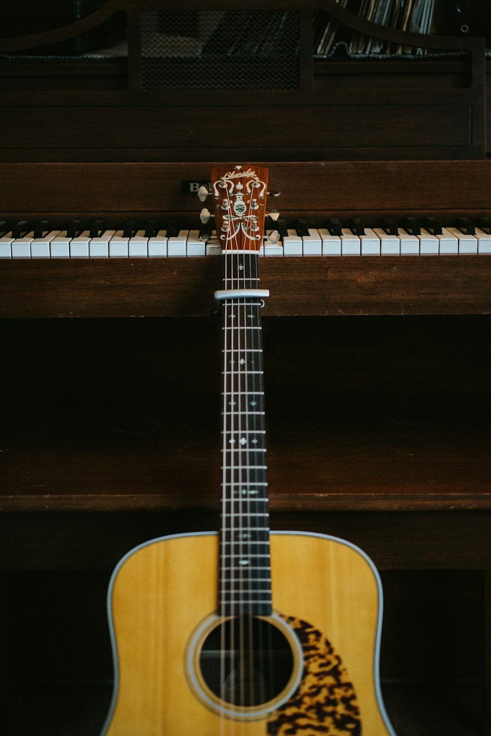 brown acoustic guitar leaning on brown piano