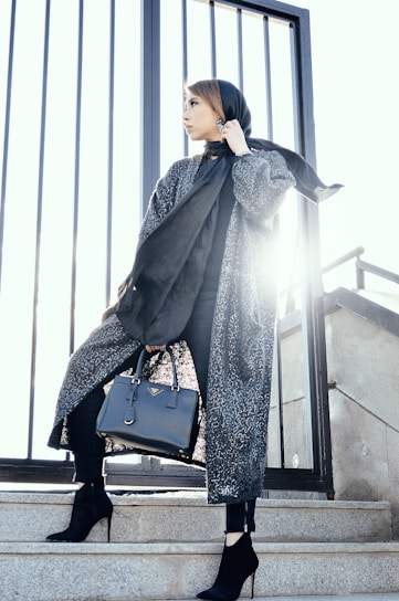 woman in gray coat holding black handbag standing on gray stairs during daytime