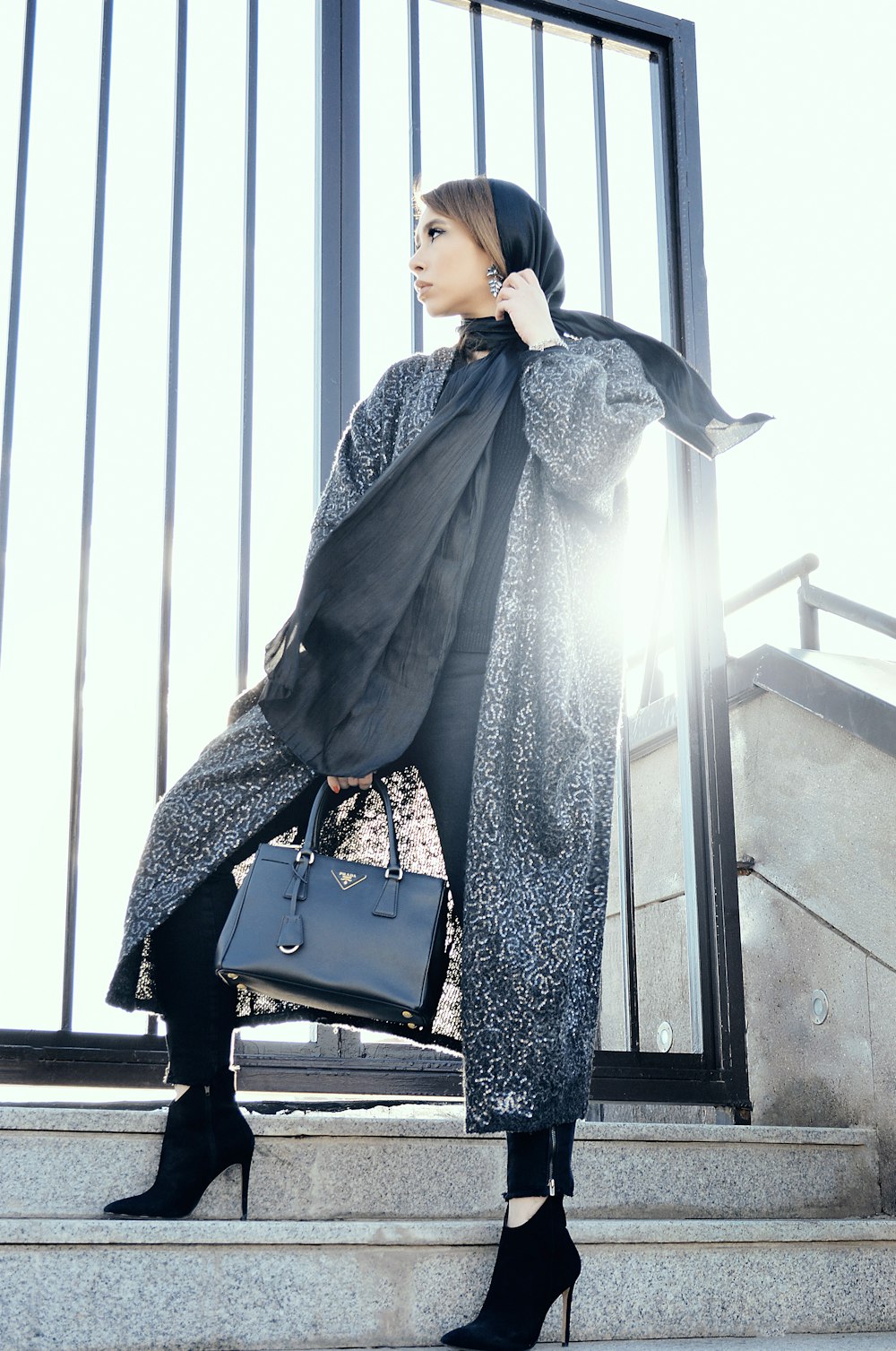 woman in gray coat holding black handbag standing on gray stairs during daytime