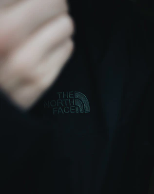 Black and white close-up of a model's hand adjusting a s-reign jacket sleeve, highlighting the embroidered logo and double stitching.