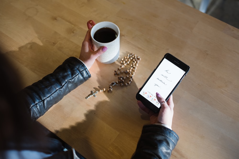 person holding smartphone and mug of coffee