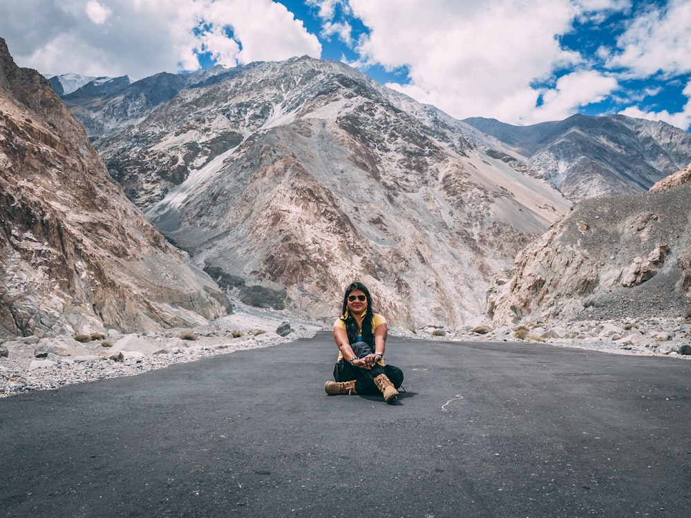 woman sitting on road near mountain during daytime