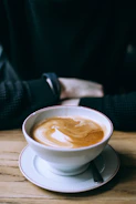 Close-up of a steaming cup of coffee on a rustic wooden table with tarot cards beside it.