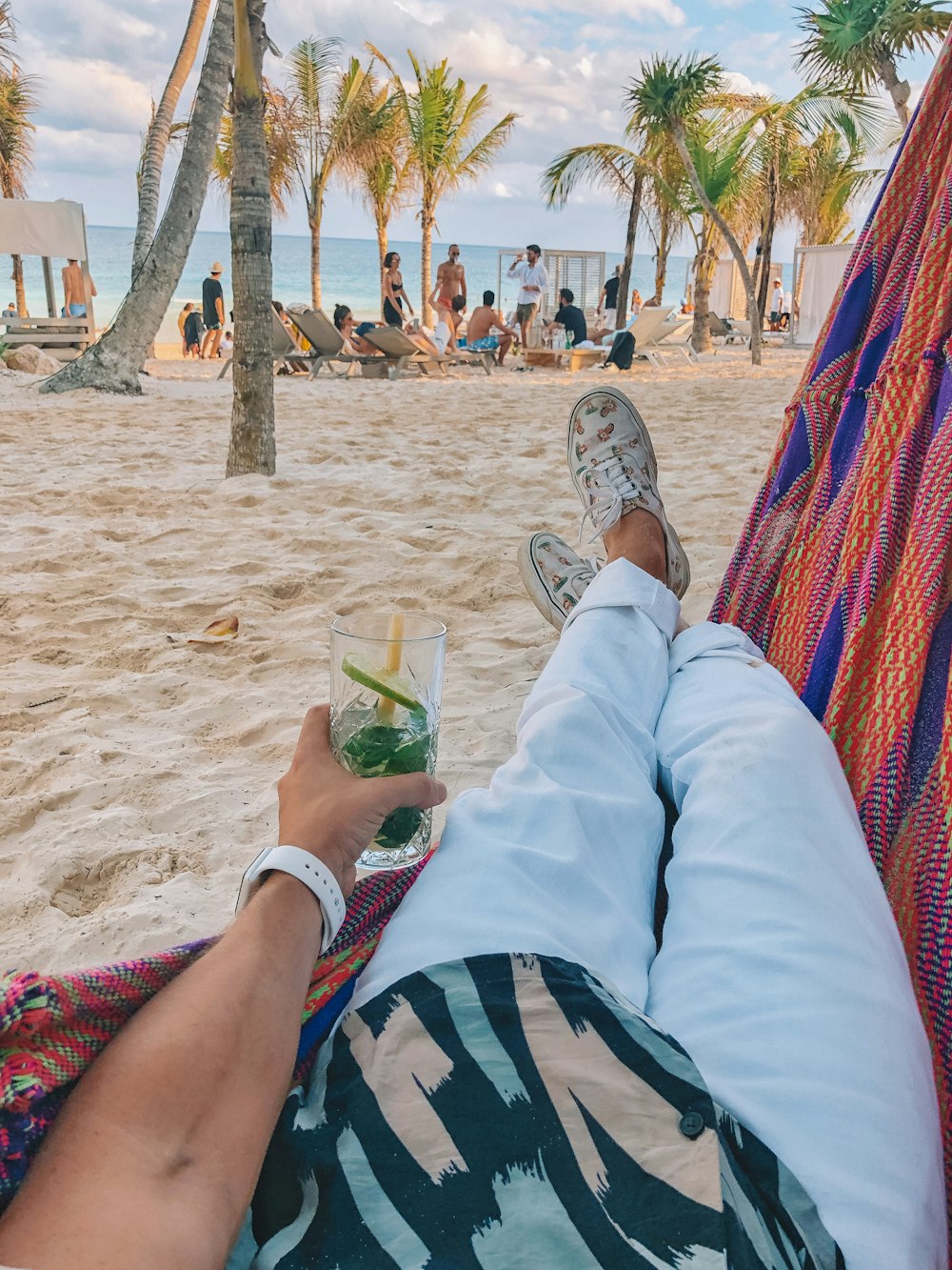 person in white pants lying on blue and red hammock