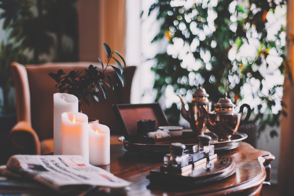 gray stainless steel tea set near three lighted pillar candles and newspaper on table