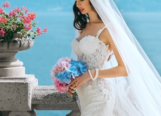 woman in wedding dress while holding flower during daytime