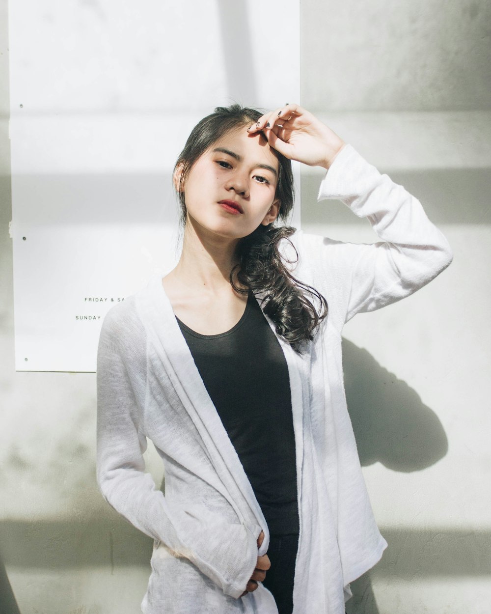 woman in white cardigan standing near white painted wall