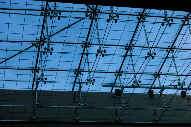 Photograph of skilled workers installing a glass enclosure with a deep blue tinted frame under natural light.