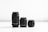 Three camera lenses of varying sizes are arranged side by side on a smooth, reflective surface against a plain white background. The tallest lens is on the left, with two progressively shorter lenses to the right. The lenses are black and cylindrical, featuring ridged focus rings and caps.