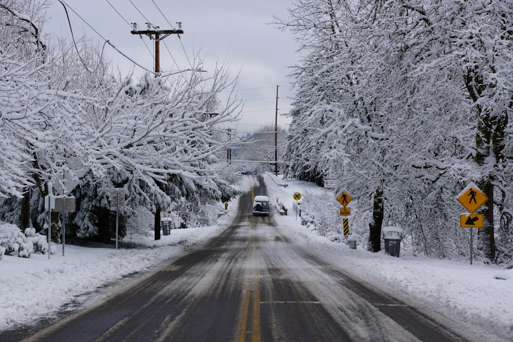 vehicle passing road between snow covered trees during daytime