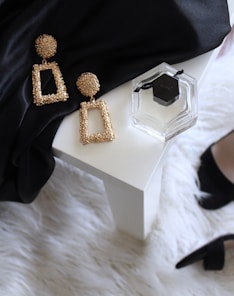 pair of gold-colored earrings on table and black ankle-strap pumps on area rug