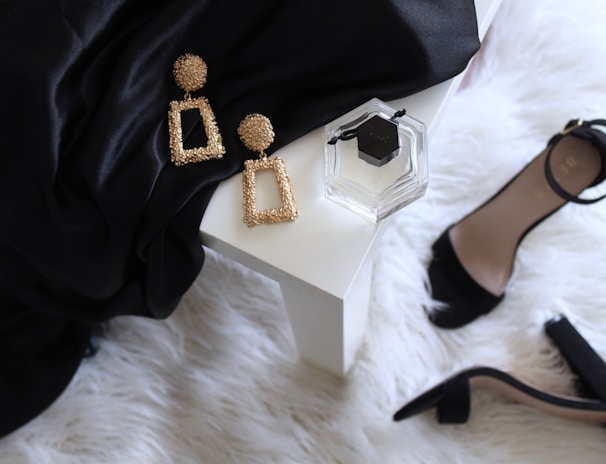 pair of gold-colored earrings on table and black ankle-strap pumps on area rug