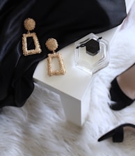 pair of gold-colored earrings on table and black ankle-strap pumps on area rug