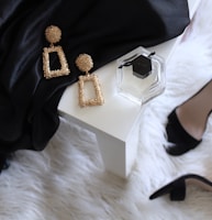 pair of gold-colored earrings on table and black ankle-strap pumps on area rug