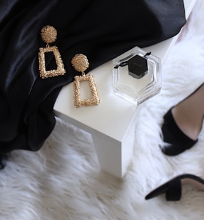 pair of gold-colored earrings on table and black ankle-strap pumps on area rug