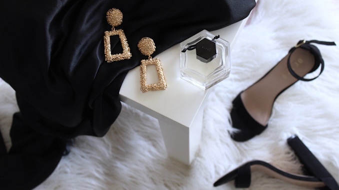 pair of gold-colored earrings on table and black ankle-strap pumps on area rug