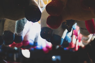 A collection of colorful hanging plush toys with bright lighting accentuating their varied colors. The background is dark, creating contrast with the illuminated plush toys.