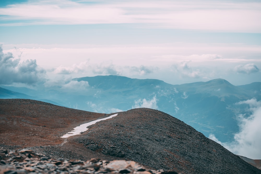 cliff overlooking clouds surrounding mountain during daytime