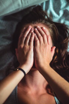 woman covering face lying on gray bed