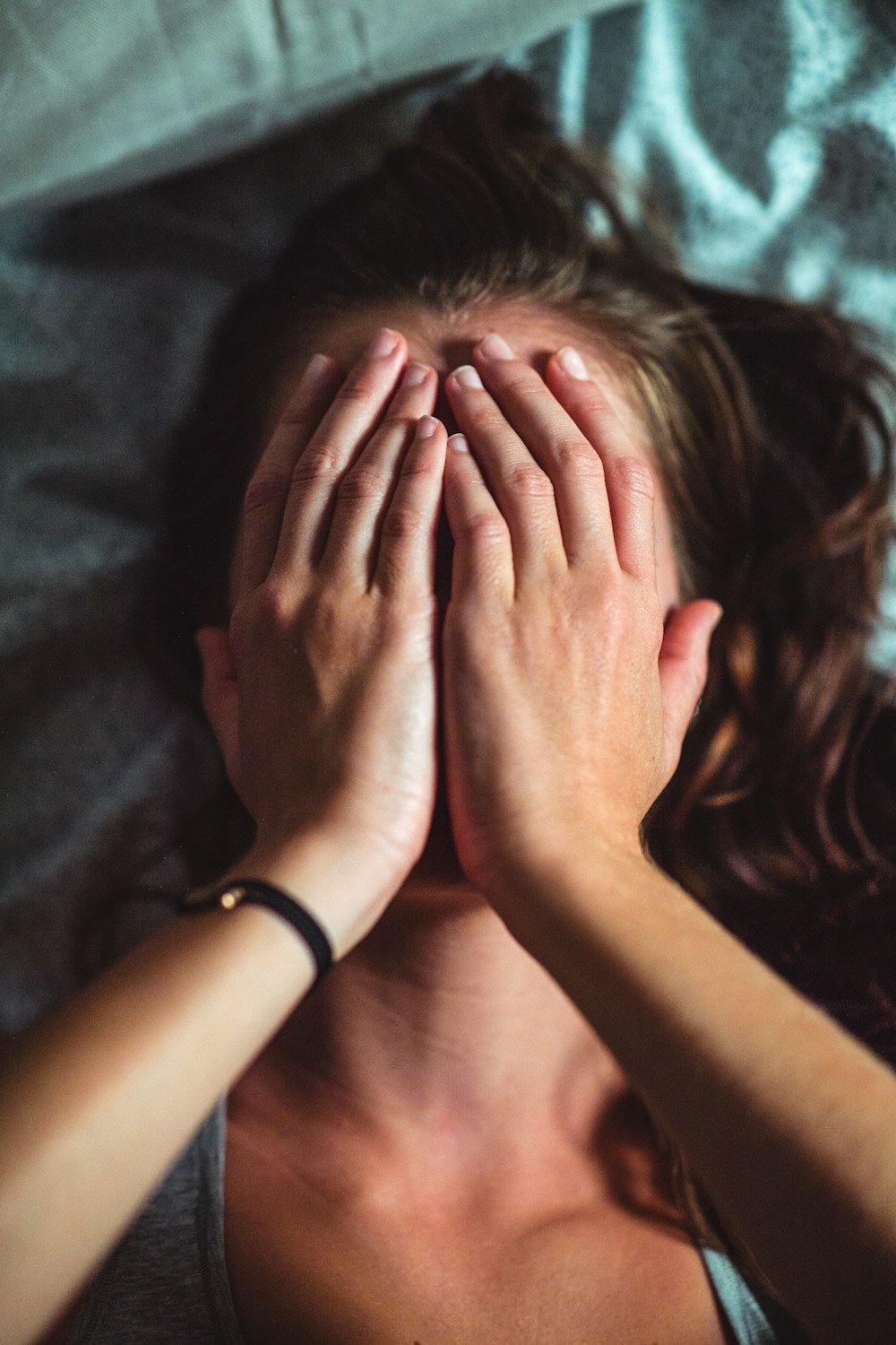 woman covering face lying on gray bed