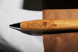 A bamboo pen engraved with the text 'ENERG3.me' is placed on a brown surface, with a metal tip visible. The grain and texture of the bamboo give it a natural look.