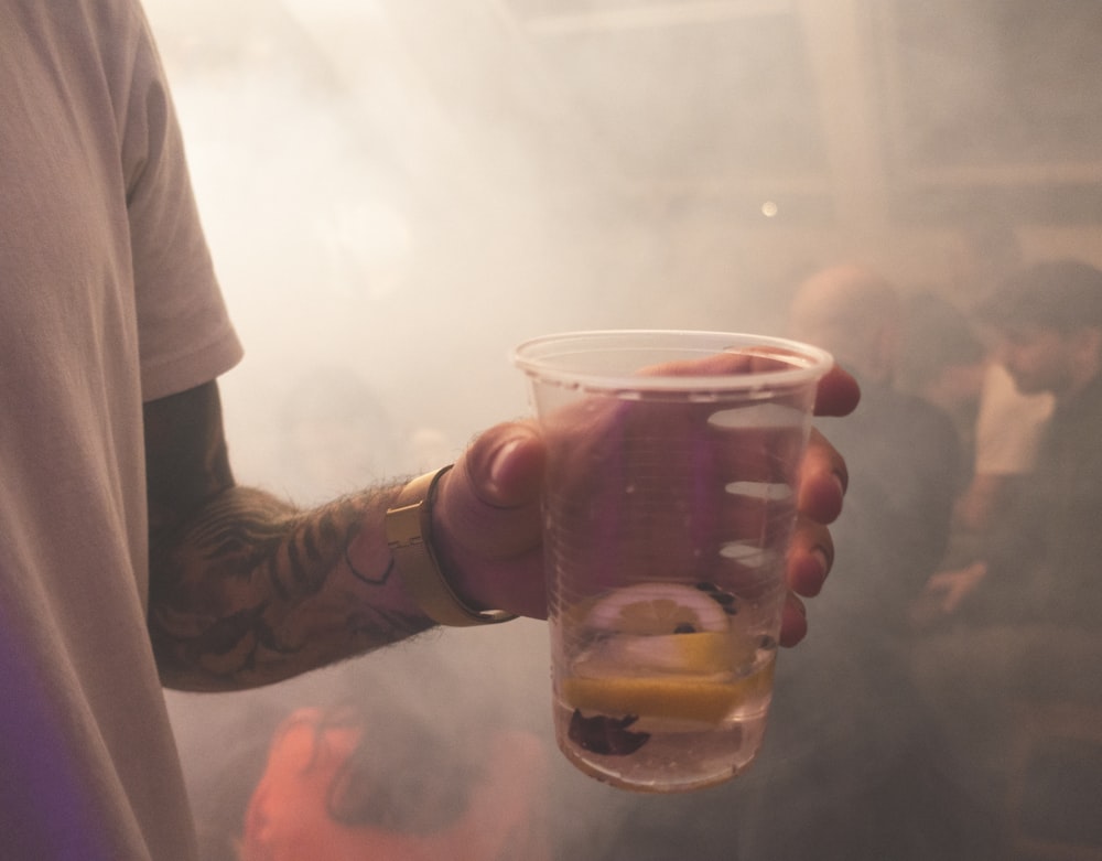 person holds plastic cup with sliced lemon