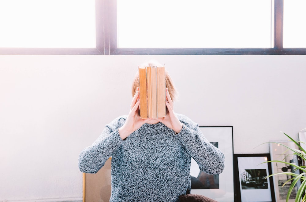 woman holding books near white surface