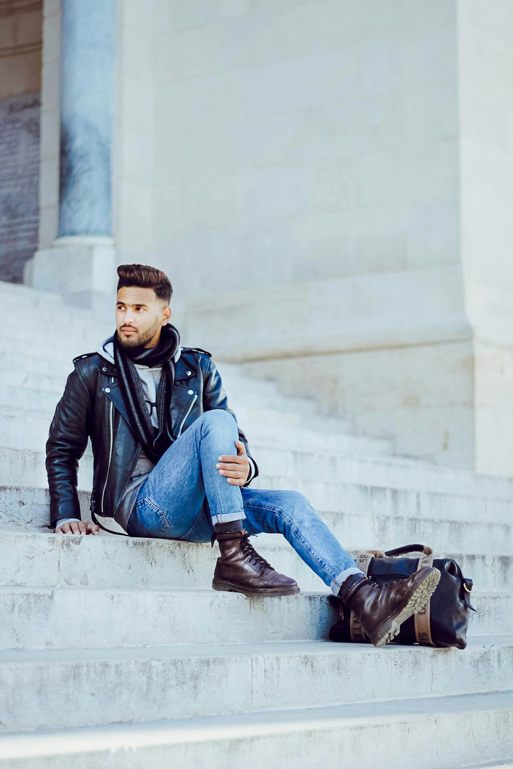 man wearing black leather jacket sitting on grey concrete stairs