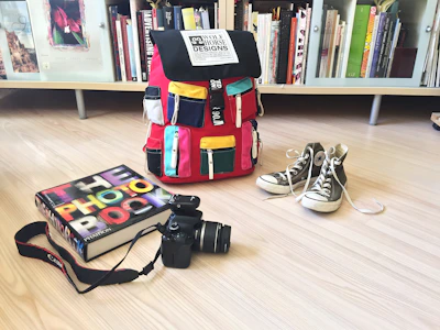 A vibrant school bag with multiple compartments, placed on a wooden desk with books.